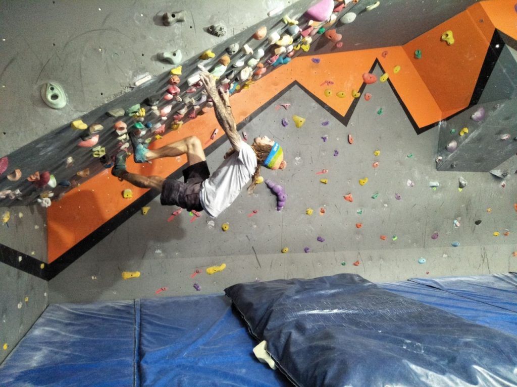 A man climbs on a steep wall in our bouldering cave at Hume with a mat positioned below him to soften his fall.
