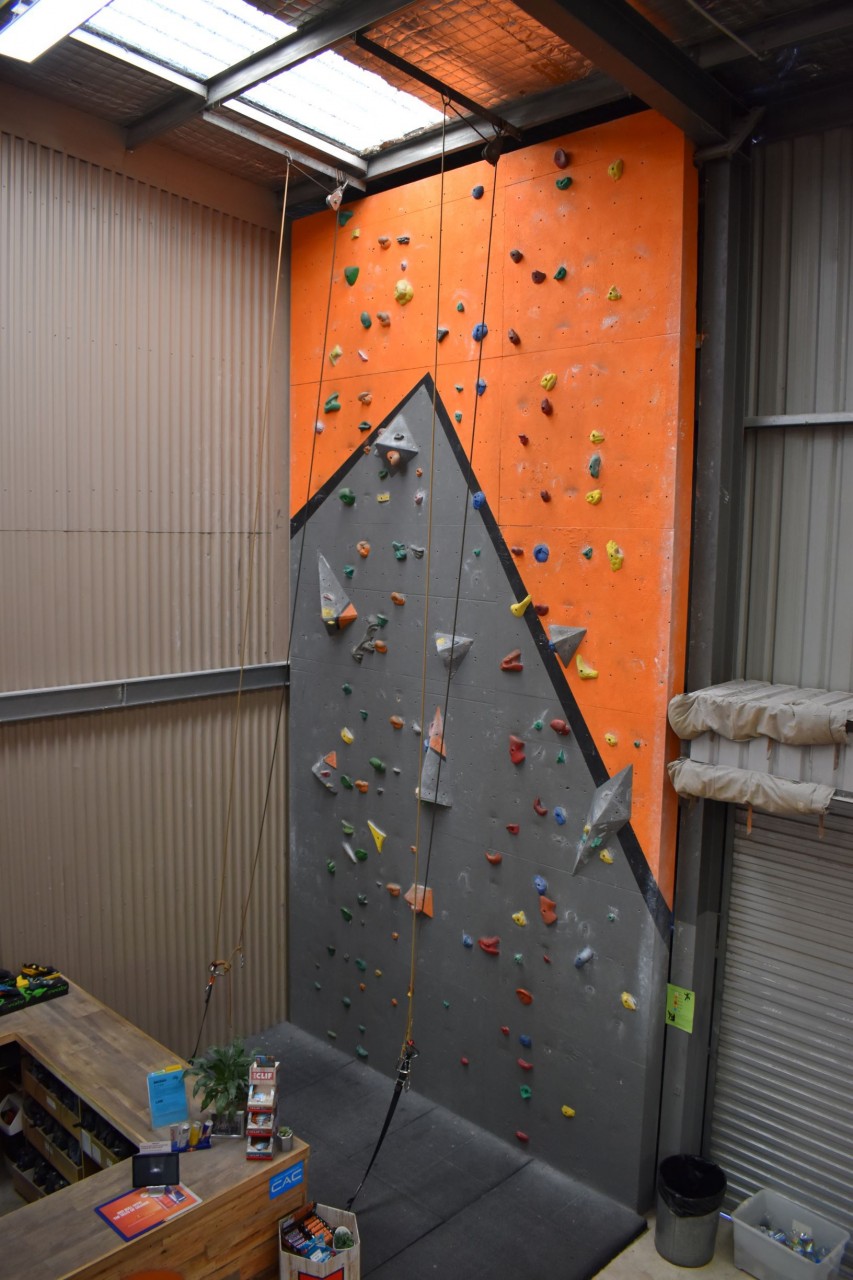 A climbing wall with two ropes directly adjacent to the front counter. Also visible: our roller doors, which are opened during the warm months to allow additional airflow.
