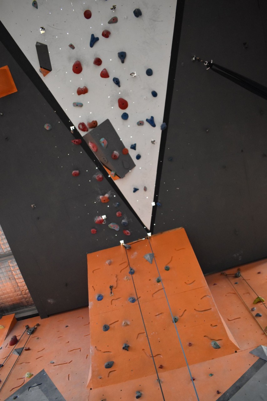 At the top of our slab wall, lead climbers can access the roof climbs. The roof climb runs along the ceiling, and is painted white, black, and grey, with some features affixed to it, and quick draws hanging down.