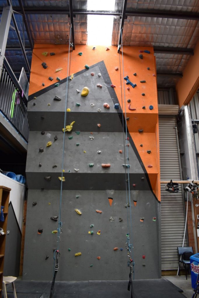 A climbing wall with two ropes and a stepped incline to the left of the front counter.