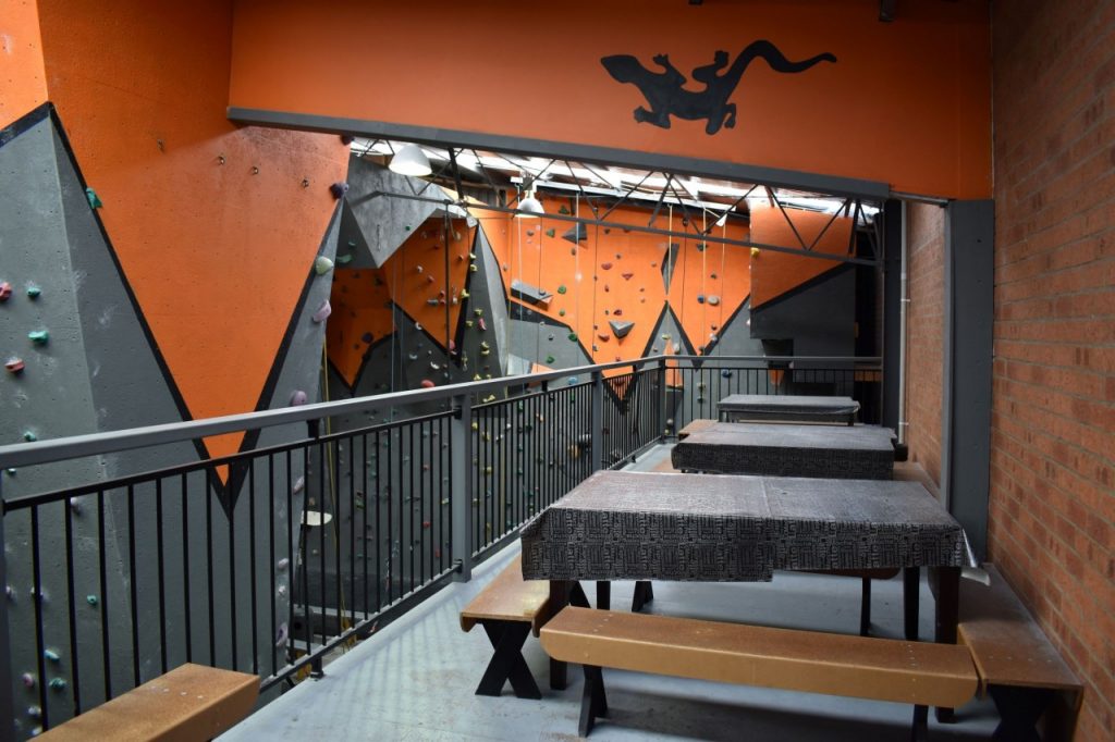 Three tables with wooden benches are lined up on the upstairs balcony, with a lovely overlook of the climbing area. A black gecko is painted on a wall over the tables.