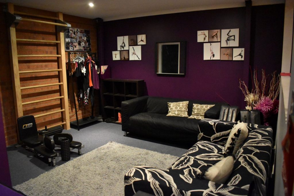 The pole studio's lounge areas includes some more training equipment, and coat rack, two black couches, and walls covered in photography of pole dancers and art.
