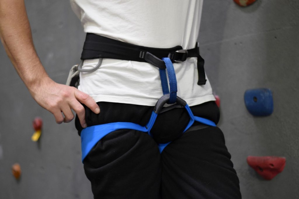 A man models Black Diamond men's Solution harness. The leg straps are blue and do not adjust, and the waist strap is black with grey detail.