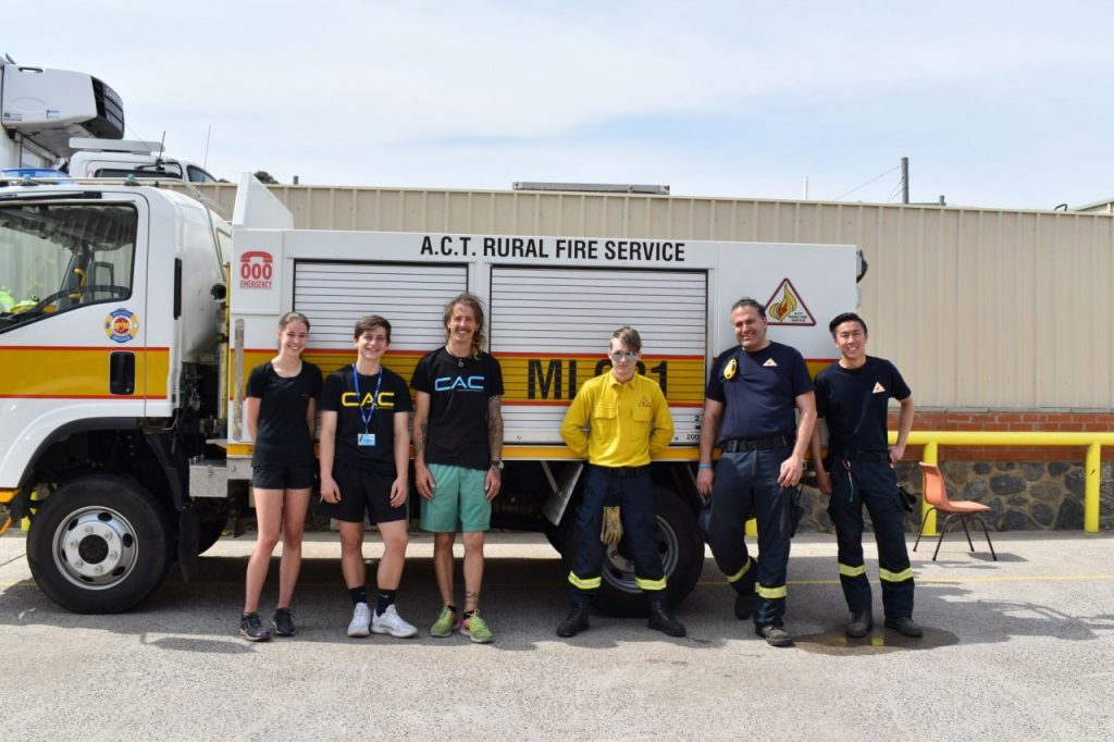 Three Canberra Indoor Rock Climbing staff and three members of the Molonglo Brigade pose in front of an ACT Rural Fire Service firetruck.